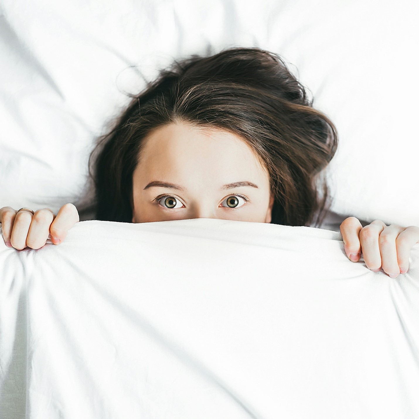 A young lady peering over a bedsheet.