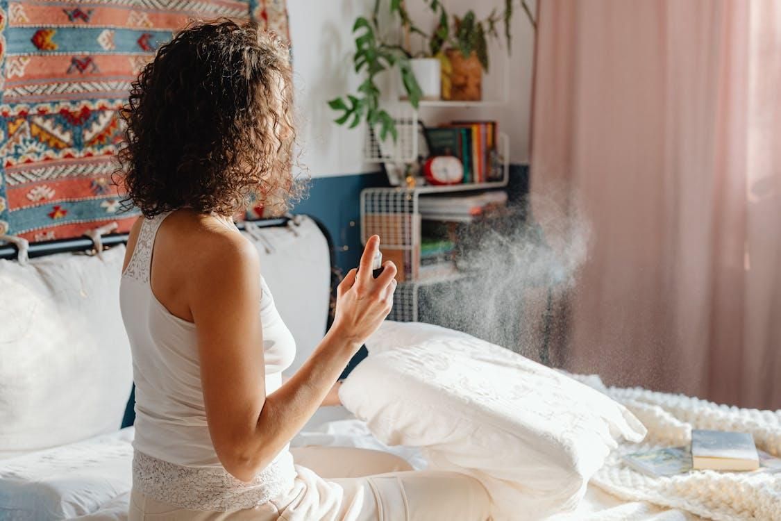 A woman spraying insect spray over her bed.